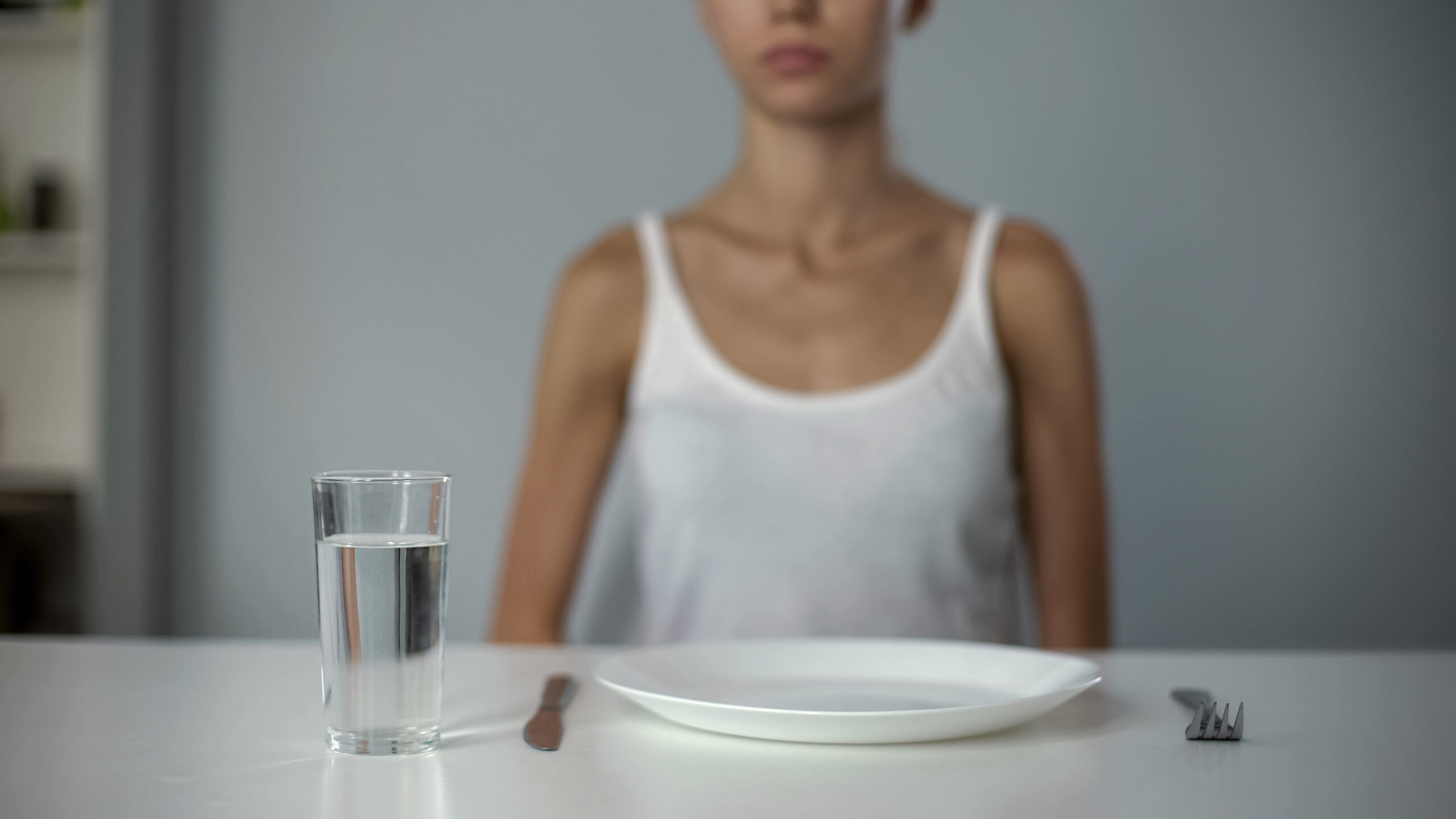 Anorexic girl sitting in front of empty plate, drinking water, severe diet